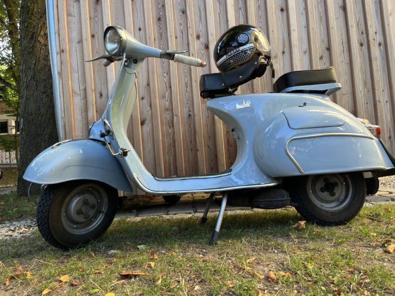 Hellblaue Vespa vor einer Holzwand
